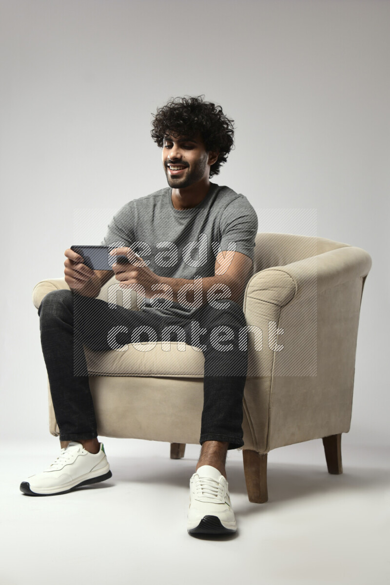 A man wearing casual sitting on a chair gaming on the phone on white background