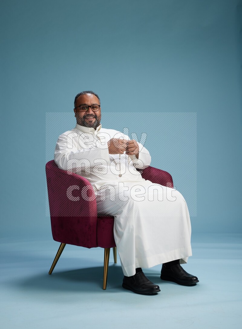 Saudi Man without shimag sitting on chair Interacting with the camera on blue background
