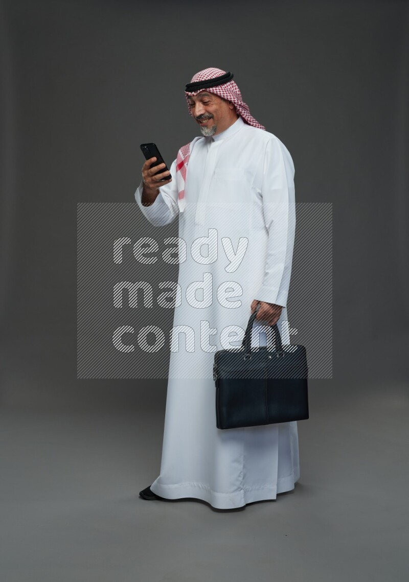 Saudi man with shomag Standing holding bag and phone on gray background