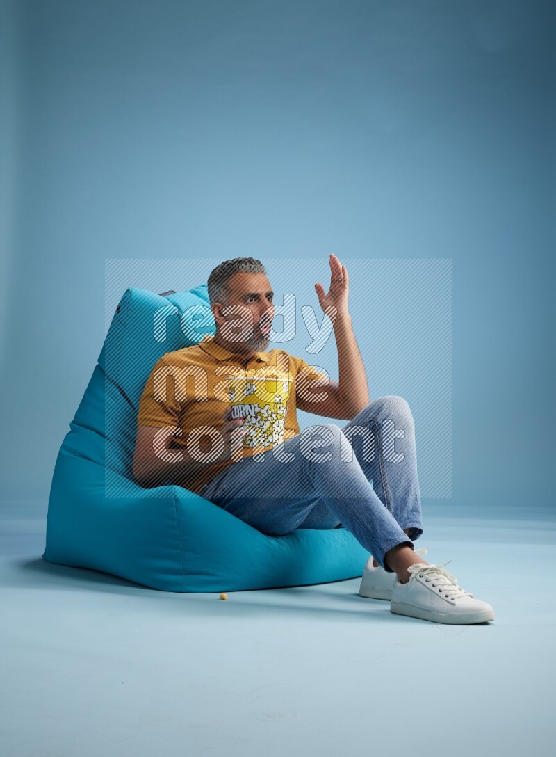 A man sitting on a blue beanbag and eating popcorn
