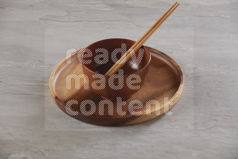 brown wood round bowl on top of brown wood round plate and wood chopsticks, on grey textured countertop