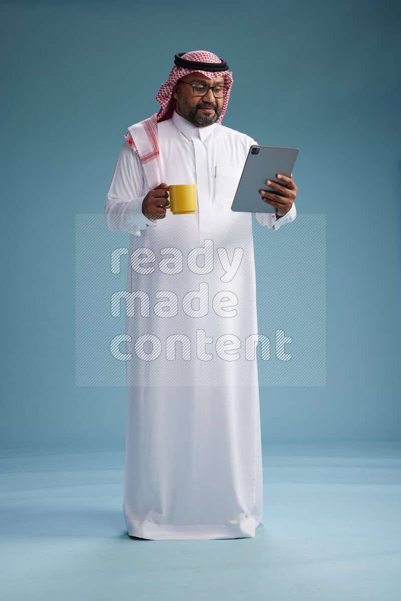 Saudi Man with shimag Standing holding a tablet on blue background