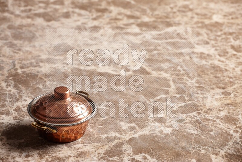 A small copper pot on beige marble background