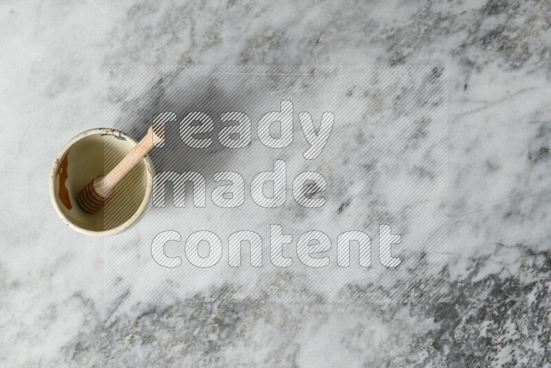 Decorative pottery bowl with wooden honey dipper in it on grey marble background