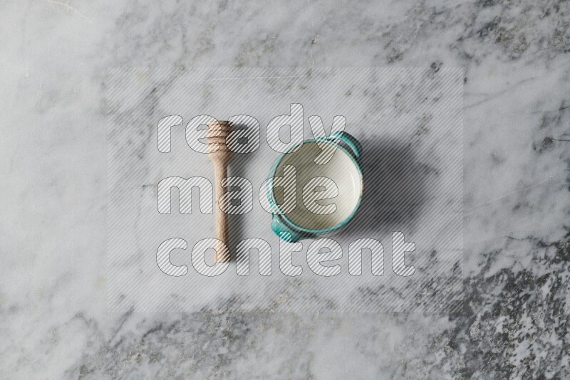 Multicolored pottery bowl with wooden honey dipper on the side on grey marble background