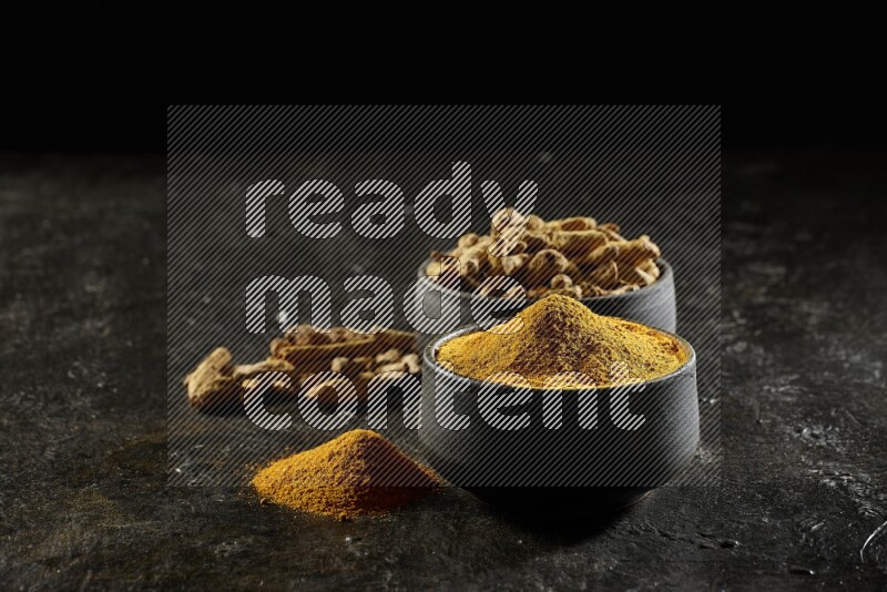 وعاءان من الفخار باللون الأسود، أحدهما ممتلئ ببودرة الكركم والآخر ممتلئ بأصابع كاملة من الكركم المجفف على خلفية سوداء