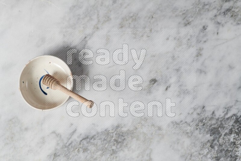 Multicolored pottery bowl with wooden honey dipper in it on grey marble background