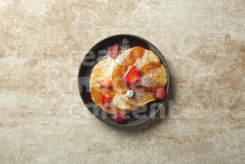Three stacked mixed berries pancakes in a black plate on beige background