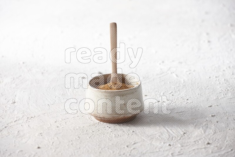 Ceramic beige bowl full of cinnamon powder with a wooden spoon on a textured white background