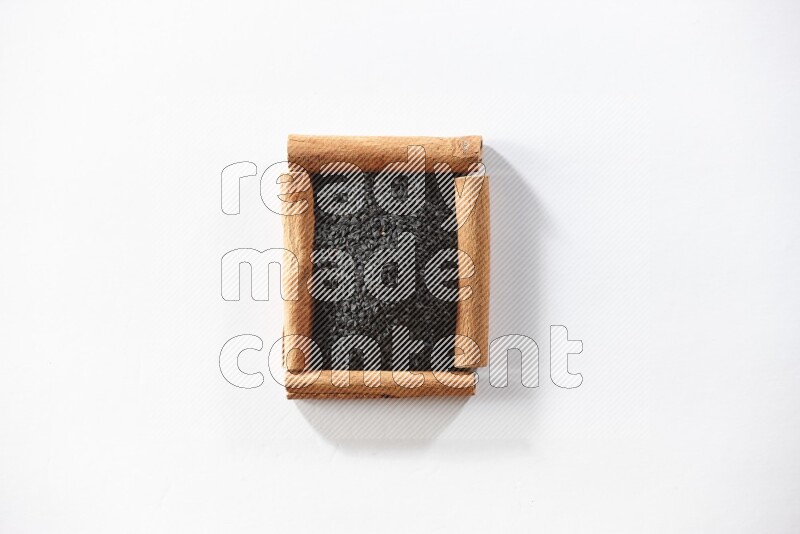 أربعة من أعواد القرفة مكونة شكل مربع بداخلها حبة البركة علي خلفية بيضاء