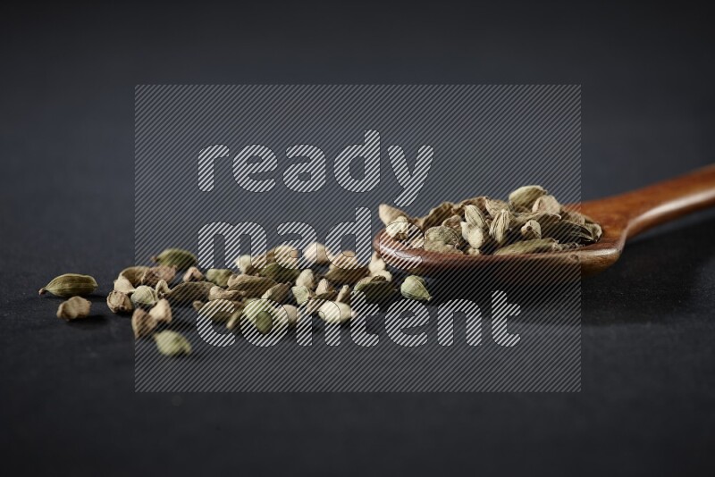 A wooden ladle full of cardamom on black flooring