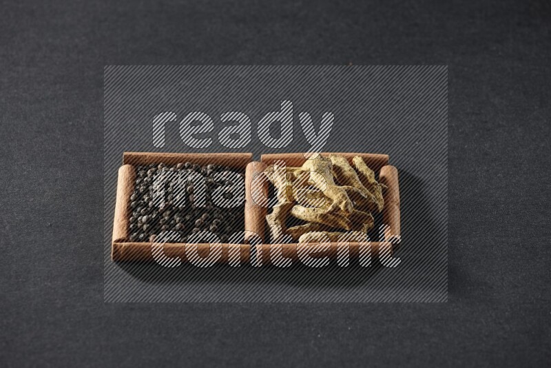 مربعان من أعواد القرفة ممتلئان بحبوب الفلفل الأسود وأصابع الكركم علي خلفية سوداء