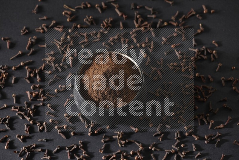 وعاء فخاري أسود ممتلئ ببودرة القرنفل وحبوب القرنفل على خلفية سوداء