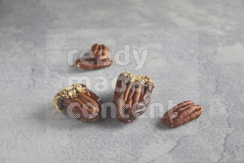 Two pecan stuffed dates covered with Dark chocolate and chopped pistachios on alight grey background