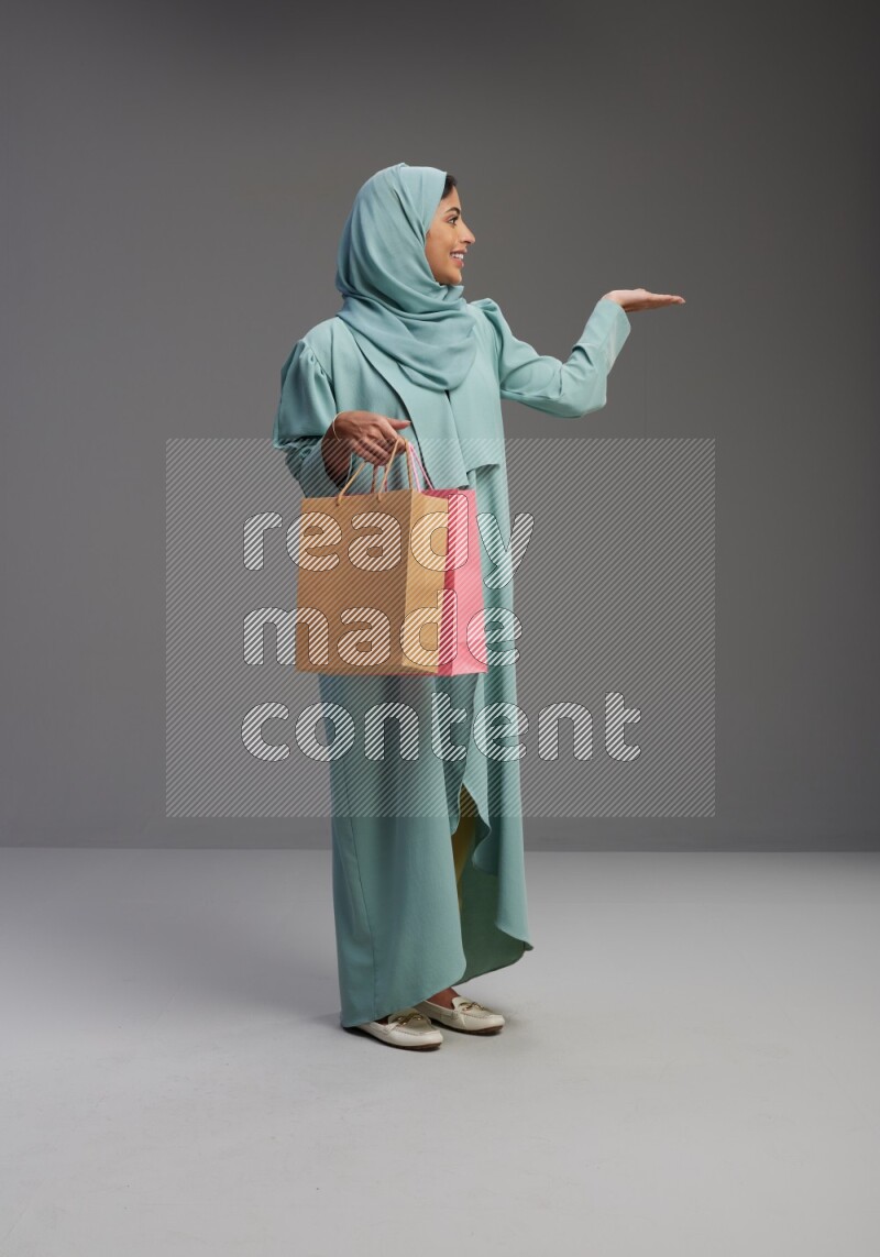 Saudi Woman wearing Abaya standing holding shopping bag on Gray background