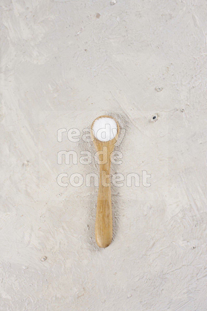 A wooden spoon full of white salt on white background