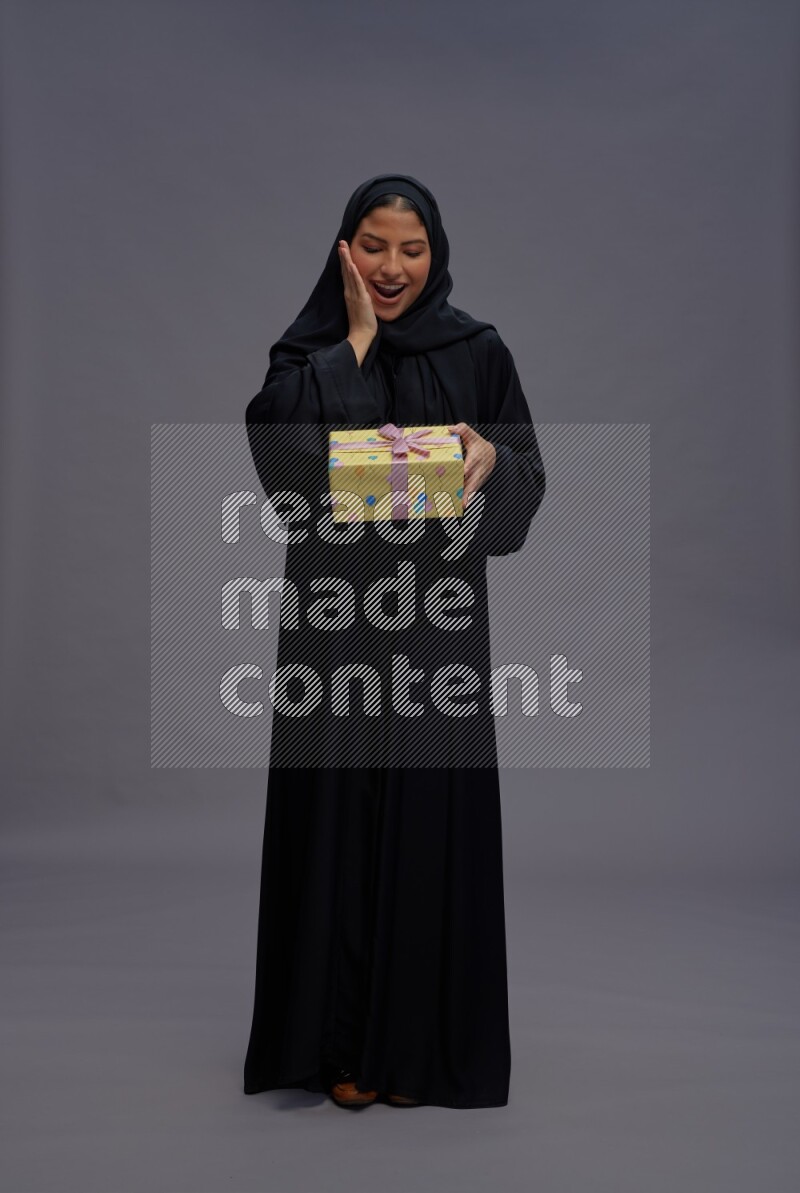 Saudi woman wearing Abaya standing holding gift box on gray background