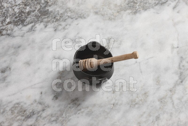 Black pottery bowl with wooden honey dipper in it on grey marble background