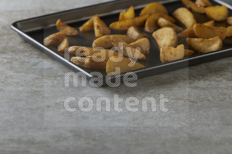 wedges potato in a black stainless steel rectangle tray on grey textured counter top