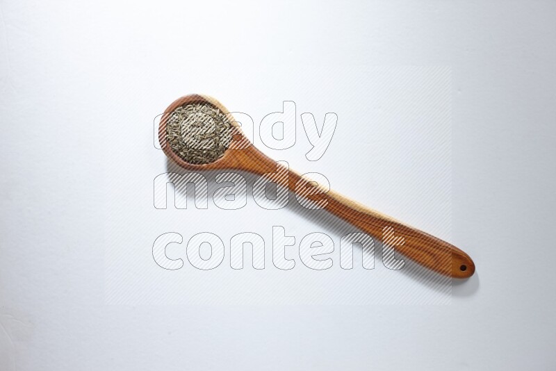 A wooden ladle full of cumin seeds on a white flooring