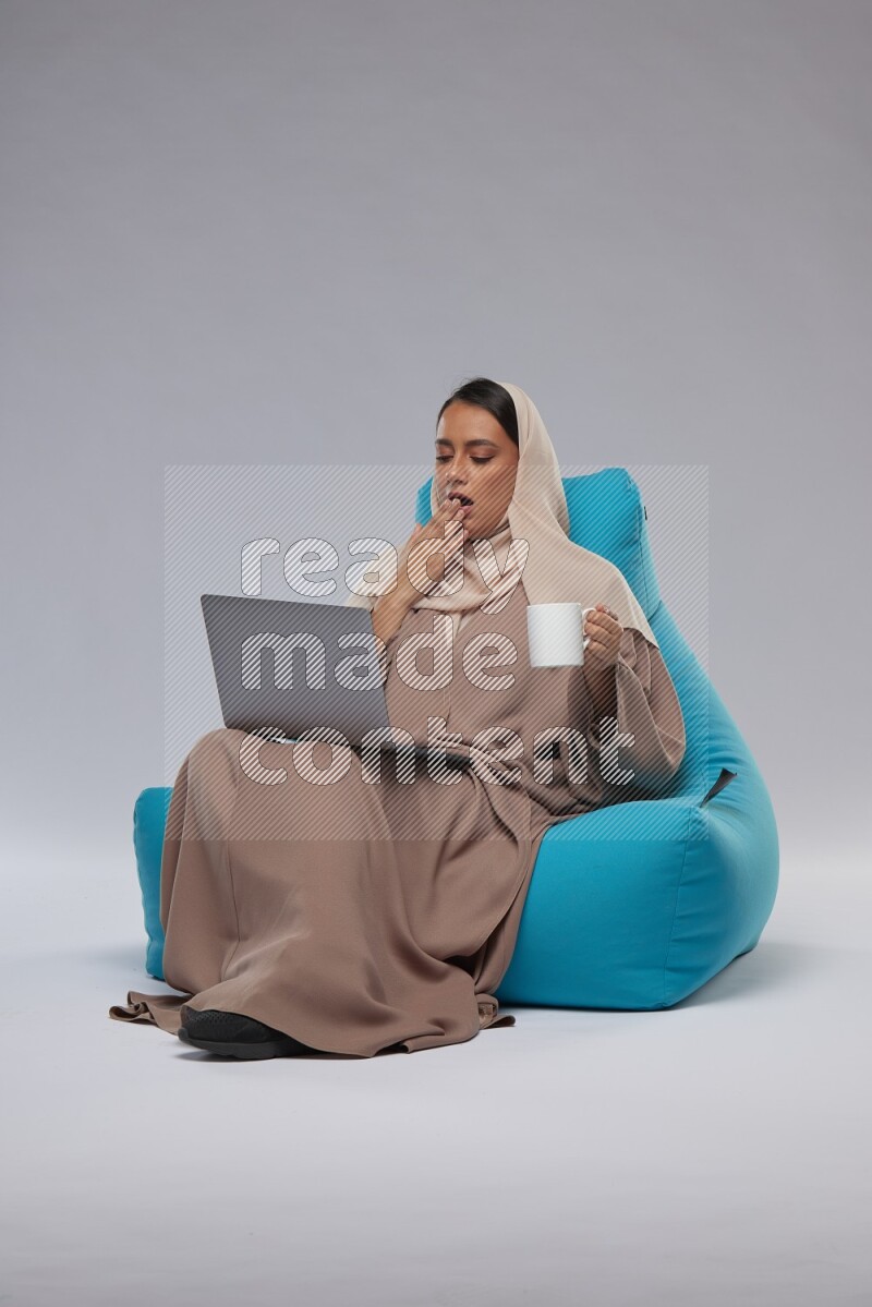 A Saudi woman sitting on a blue beanbag and working on laptop