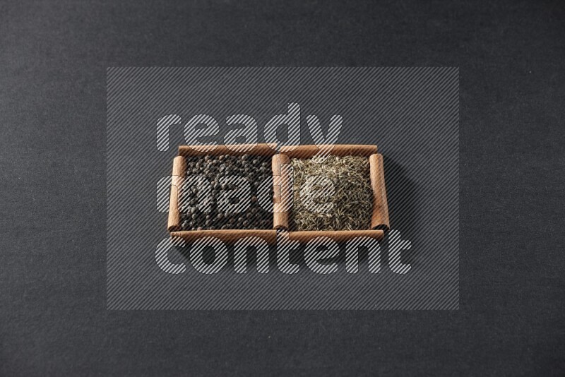 مربعان من أعواد القرفة ممتلئان بحبوب الفلفل الأسود وحبوب الكمون علي خلفية سوداء