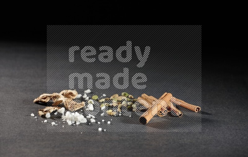 Ginger, salt, cardamom and cinnamon sticks on black flooring