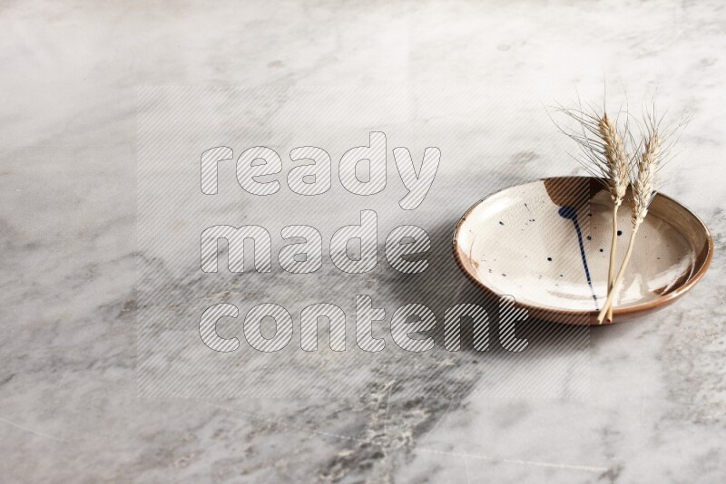 سنابل من القمح علي طبق فخاري متعدد الألوان علي خلفية من الرخام الرمادي