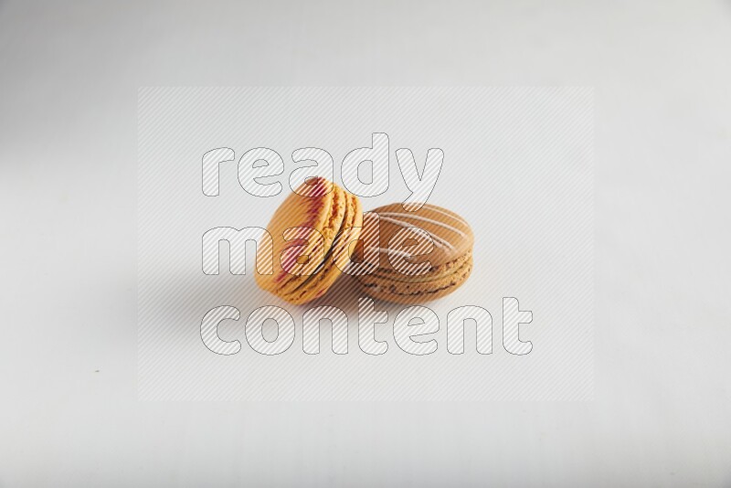 45º Shot of of two assorted Brown Irish Cream, and Orange Exotic macarons on white background