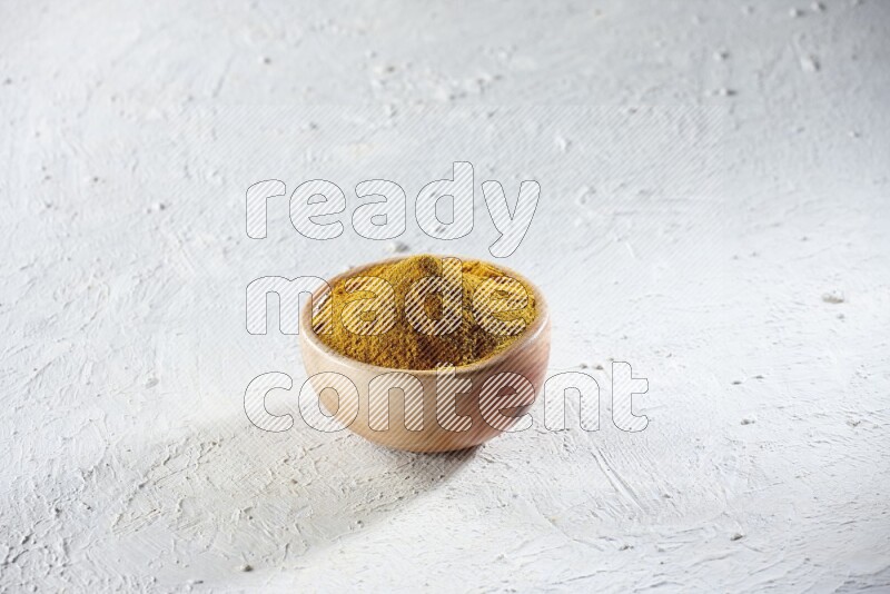 A wooden bowl full of turmeric powder on a textured white flooring