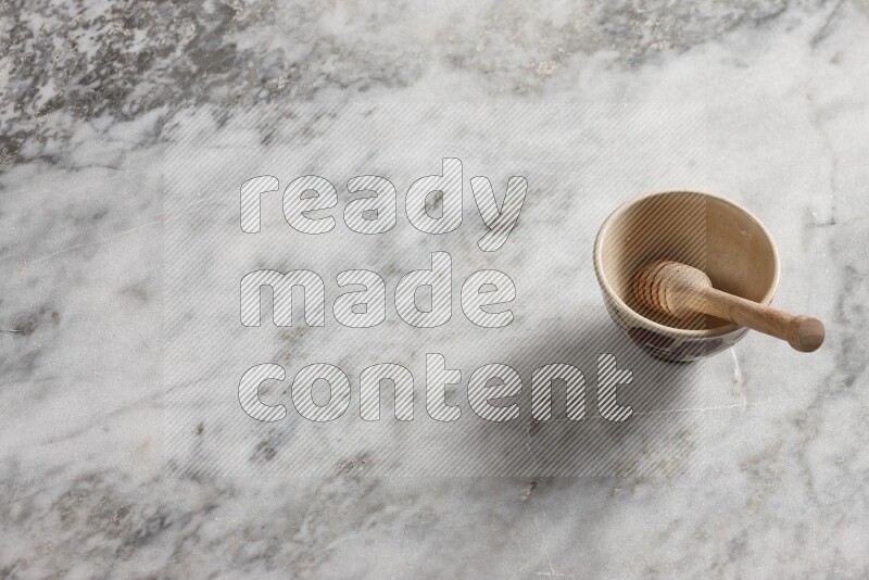 Decorative pottery bowl with wooden honey dipper in it on grey marble background
