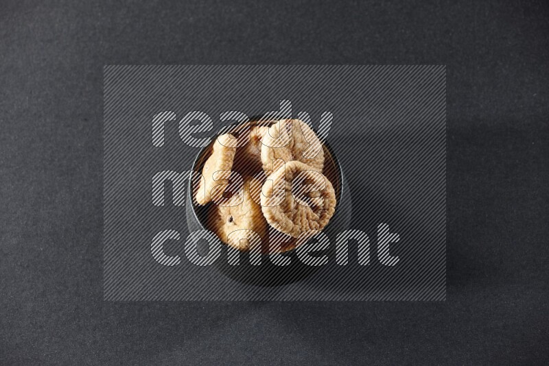 A black pottery bowl full of dried figs on a black background in different angles