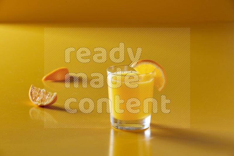 glass of orange juice with orange slice on yellow background