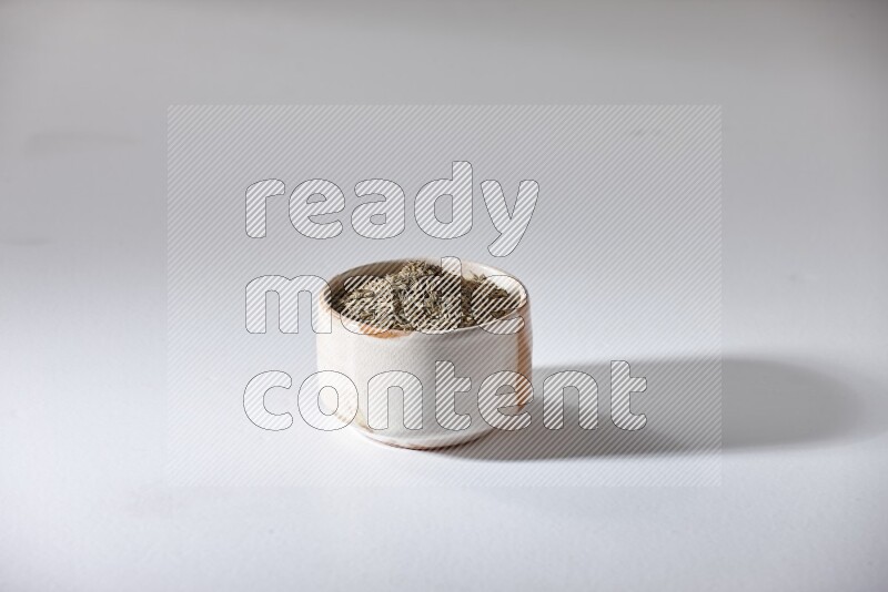 A beige bowl full of cumin seeds on a white flooring