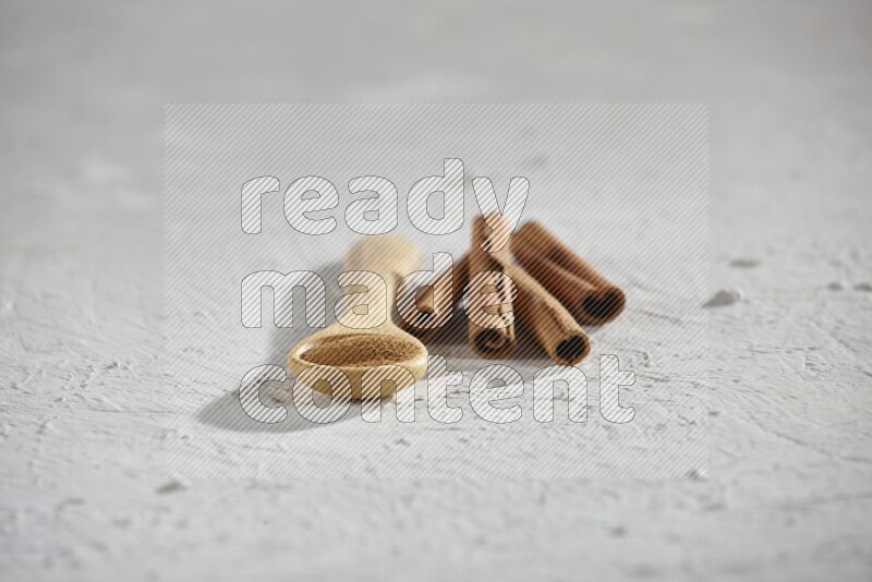 Cinnamon powder in a wooden spoon with cinnamon sticks on white background