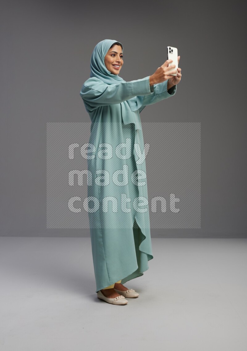 Saudi Woman wearing Abaya standing taking selfie on Gray background