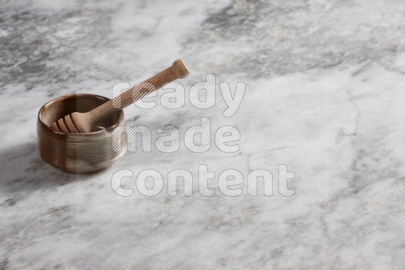 Brown pottery bowl with wooden honey dipper in it on grey marble background