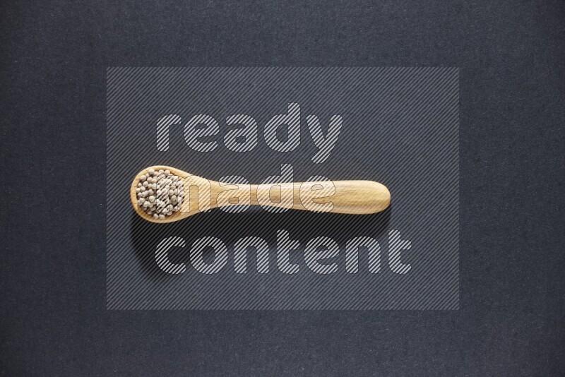 A wooden spoon full of white pepper beads on black flooring