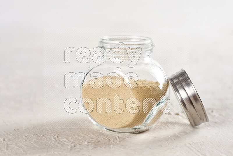A glass jar full of ground ginger powder on white background