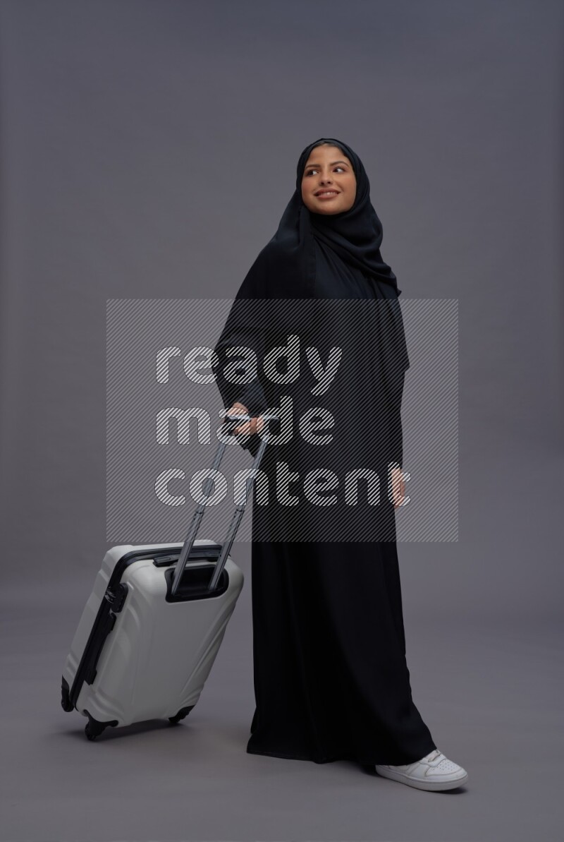 Saudi woman wearing Abaya standing holding bag on gray background