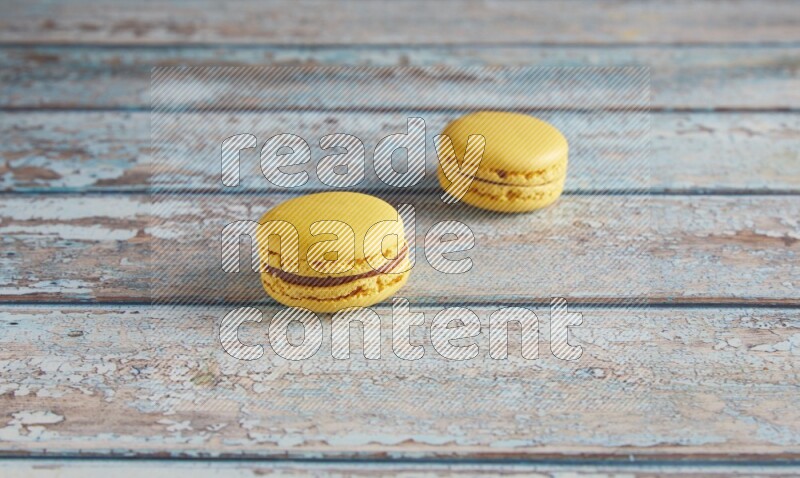45º Shot of two Yellow Lemon macarons on light blue wooden background