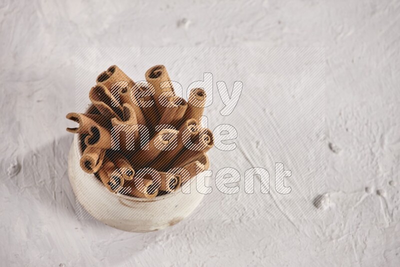 Cinnamon sticks in a beige bowl and more sticks beside it on white background