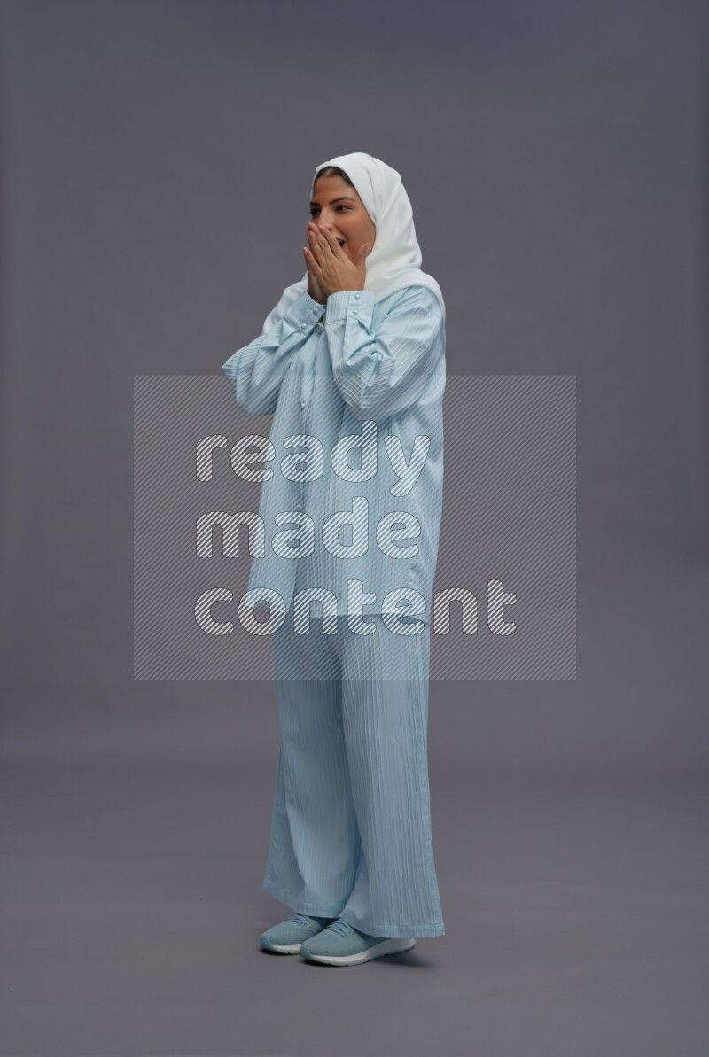 Saudi woman wearing hijab clothes standing interacting with the camera on gray background