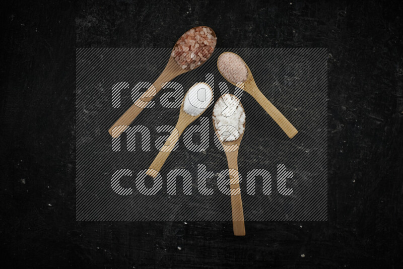 4 wooden spoons filled with fine and coarse salt on black background