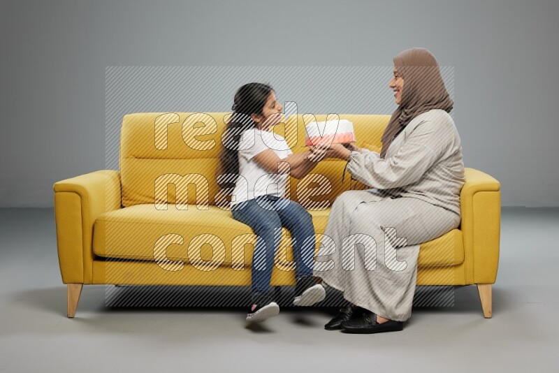 A girl sitting giving a cake to her mother on gray background