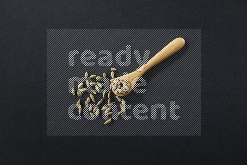 ملعقة خشبية ممتلئة بالهيل على خلفية سوداء