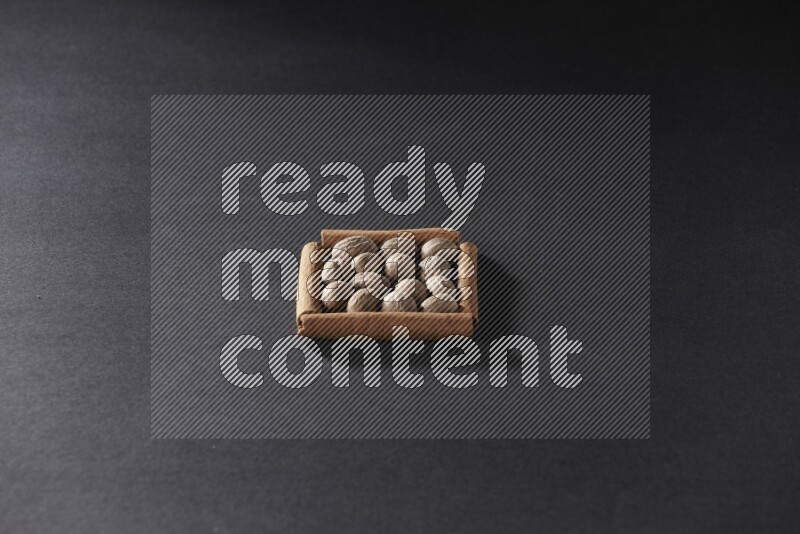 أربعة من أعواد القرفة مكونة شكل مربع بداخلها جوزة الطيب علي خلفية سوداء