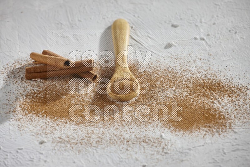 Cinnamon powder in a wooden spoon with cinnamon sticks and sprinkles powder on the flooring on white background