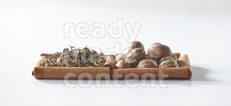 مربعان من أعواد القرفة ممتلئان بالريحان المجفف وجوزة الطيب علي خلفية بيضاء