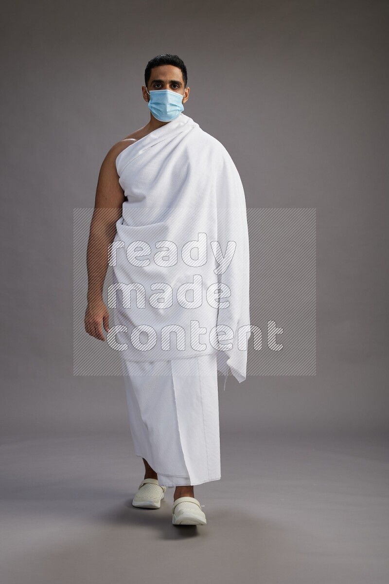 A man wearing Ehram with face mask Standing Interacting with the camera on gray background